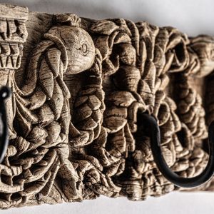 Percha Askale de estilo étnico fabricado en madera de teka en color marrón con acabado tallado combinado con hierro en color negro.