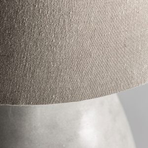 Lámpara de sobremesa de estilo contemporáneo fabricado en cemento en color blanco con acabado decapado combinado con algodón en color marrón. Producto desmontable elevable.